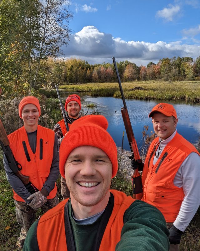 The four of us in blaze orange, shotguns over our shoulders, standing at
                 a creek in the northern Wisconsin woods on an October afternoon